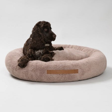 Dog sitting on a fluffy pink pet bed with a brand logo on a white background