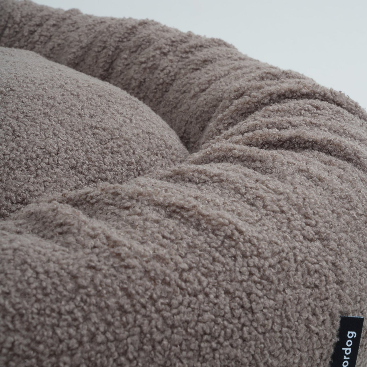 Close-up of a fluffy gray pet bed with a brand label on a light gray background