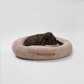 A brown round dog bed with a plush texture, featuring a lying dog resting on it.